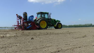 Groene tractor met zaaimachine bewerkt akkergrond voor het verbouwen van zilveruitjes en parijse wortelen